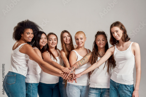 Group of diverse women showing unity, putting their hands on top of each other like a team while smiling at camera isolated over grey background