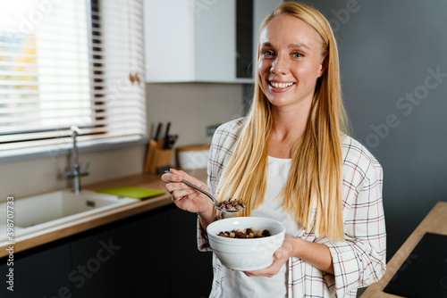 Beautiful blonde happy woman eating cereal while having breakfast