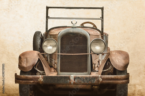 Over a century old rusted and broken classic car in front of an old wall