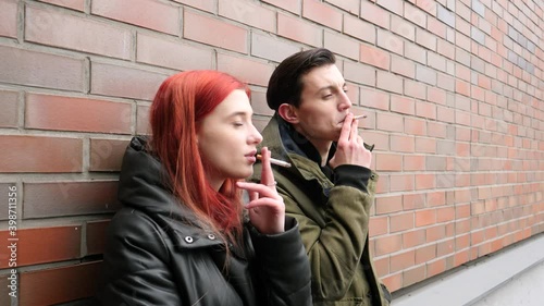 Bad habit young people couple staand smoking cigarretes exhaling dense smoke communicating leaning the wall photo