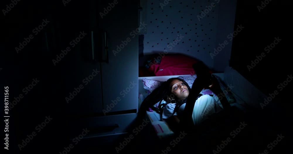 Teen black girl using cellphone device at night in bed Teen black girl using cellphone device at night in bed