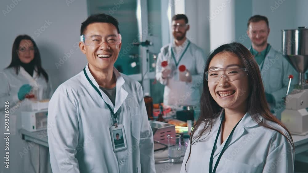 Group portrait of multi-ethnic team of professional scientists and students laughing cheerfully into camera cooperating in the laboratory.