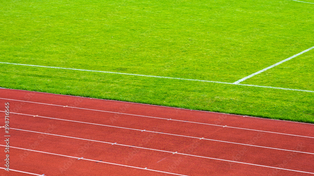 Fototapeta premium Red running track and green grass field on sports stadium.