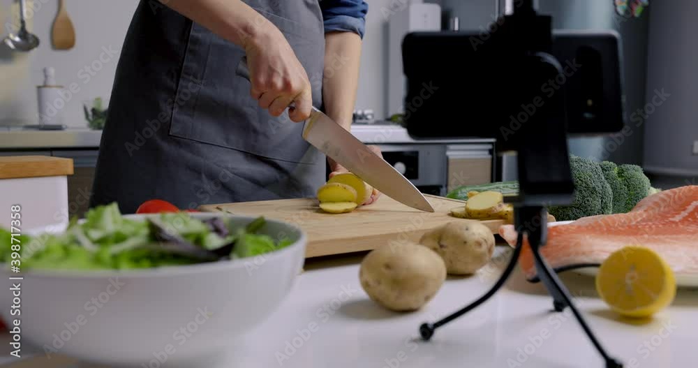 food blogger recording video with phone camera at home kitchen. cutting potato on wooden board food blogger recording video with phone camera at home kitchen. cutting potato on wooden board