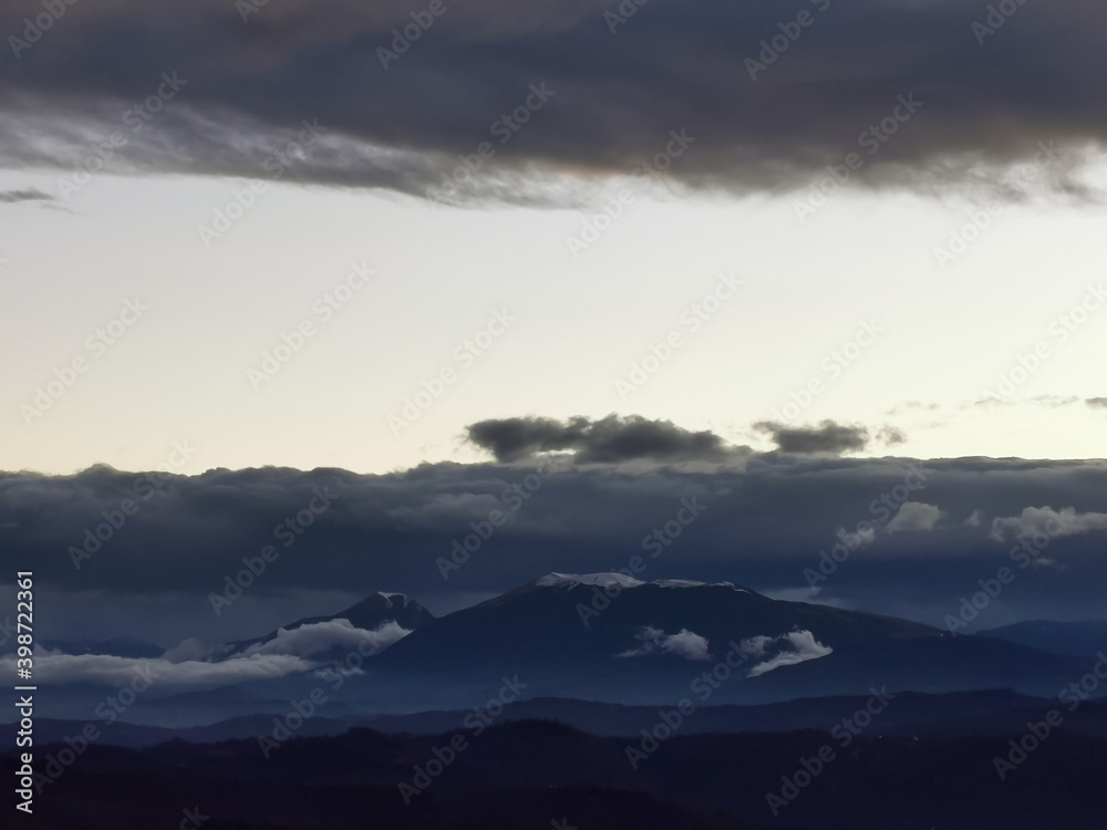 Cime innevate dei monti Appennini in un tramonto di nuvole scure e luce