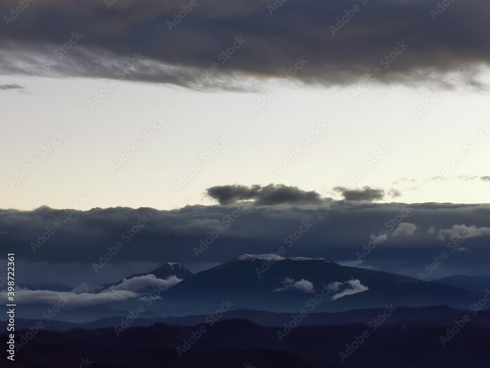 Cime innevate dei monti Appennini in un tramonto di nuvole scure e luce Cime innevate dei monti Appennini in un tramonto di nuvole scure e luce