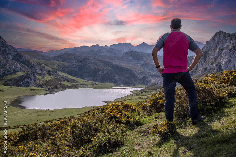 A young man looking at the beautiful Covadonga lake in Asturias in a beautiful spring sunset, Picos de Europa. Spain A young man looking at the beautiful Covadonga lake in Asturias in a beautiful spring sunset, Picos de Europa. Spain