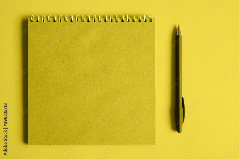 notebook or sketchbook made of craft paper and a pen on a yellow background. space for text. toned in illuminating and ultimate gray, trend color of the year 2021 notebook or sketchbook made of craft paper and a pen on a yellow background. space for text. toned in illuminating and ultimate gray, trend color of the year 2021