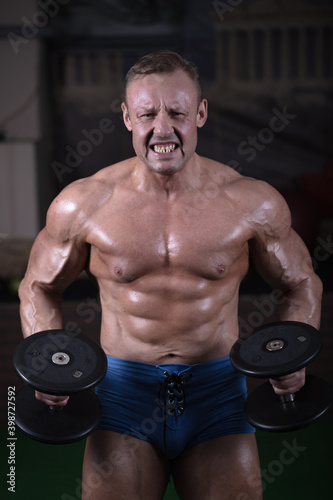 A man goes in for sports in the gym and trains his muscles. Bodybuilder works out with dumbbells