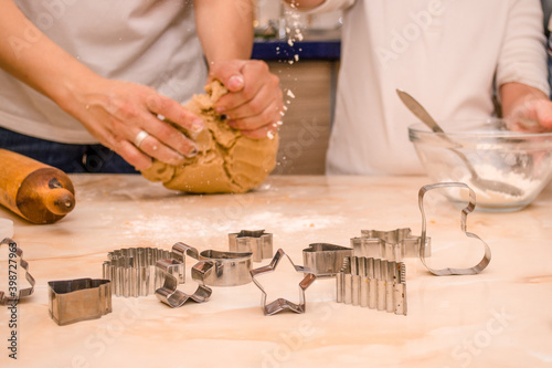 Hands of mother and daughter prepare festive gingerbread cookies for christmas, daughter pours flour on dough photo