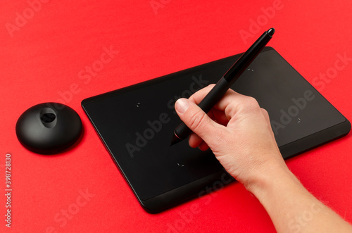 Fototapet Closeup of woman hand, stylus and black graphics tablet on the red surface