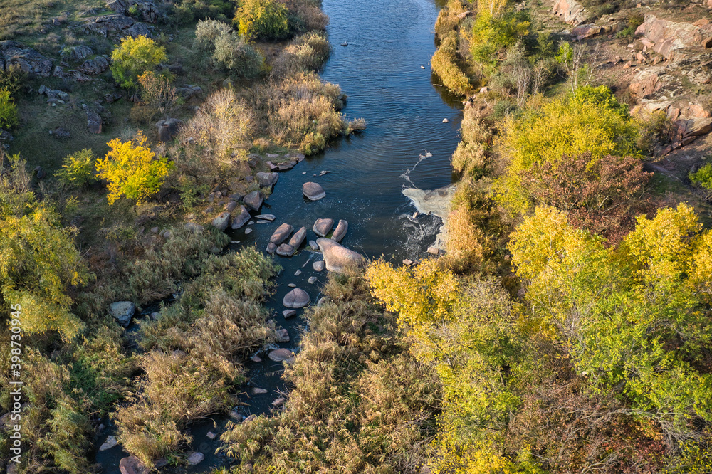 A picturesque stream flows in the Aktovsky Canyon, surrounded by autumn trees and large stone boulders A picturesque stream flows in the Aktovsky Canyon, surrounded by autumn trees and large stone boulders
