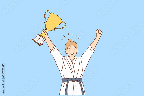 Girl karate fighter and winner concept. Smiling happy girl in white kimono with belt karate fighter standing with golden trophy in hands and celebrating victory feeling confident 