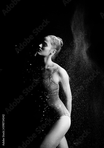 A high contrast photo of a ballet dancer girl wearing a bodysuit with flour flying around her body on a black background. Artistic, commercial, monochrome design
