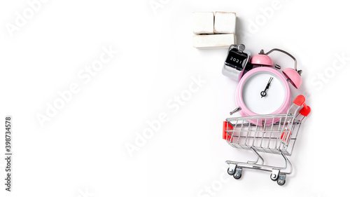 alarm clock in a pink plastic case and black hands in a metal shopping cart with tally click counter on a white background selective focus isolated