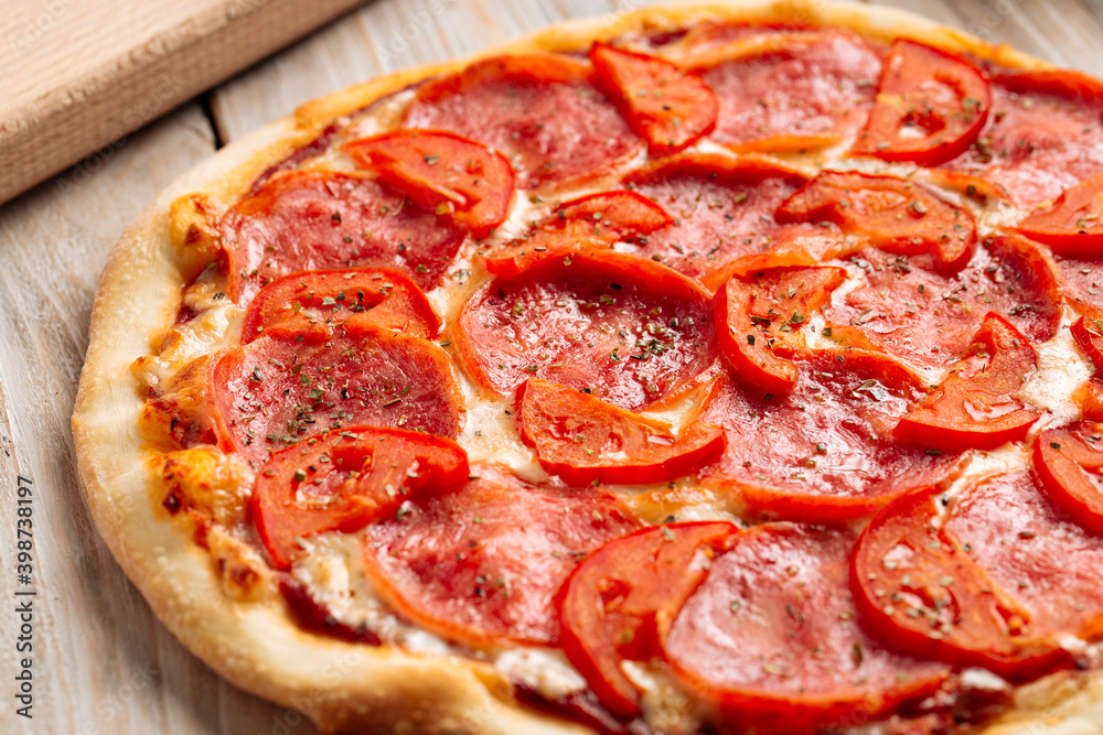 Closeup on ham pizza with tomato with dried herbs on the wooden table Closeup on ham pizza with tomato with dried herbs on the wooden table
