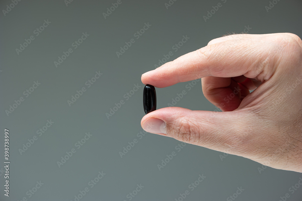 Caucasian male hand holding a black medicine capsule pill between fingers close up shot isolated studio shot Caucasian male hand holding a black medicine capsule pill between fingers close up shot isolated studio shot
