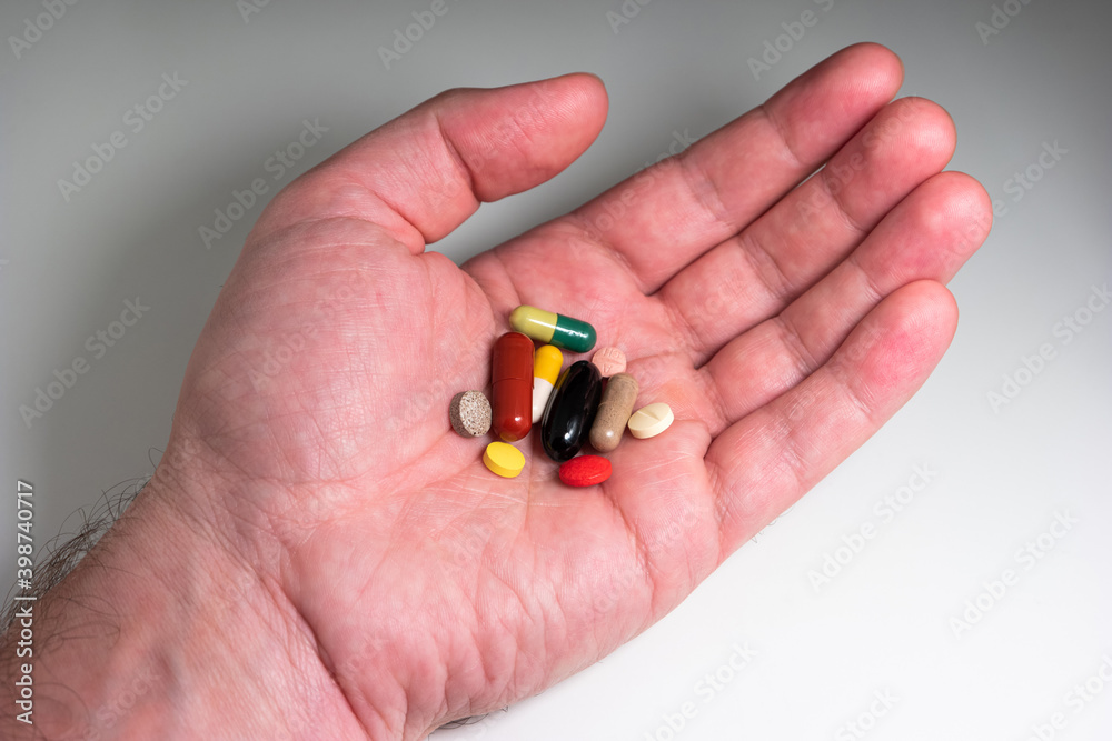 Caucasian male hand holding a variety of colored medical and supplements capsules and pills isolated on white top view Caucasian male hand holding a variety of colored medical and supplements capsules and pills isolated on white top view