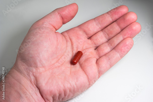 Caucasian male hand holding a red medical capsule pill isolated on white top view