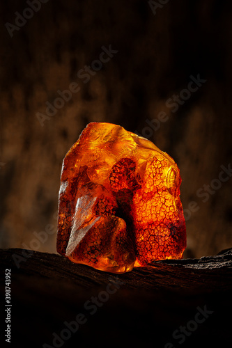 Beauty of natural raw amber. A piece of yellow and red semi transparent natural amber on piece of stoned wood.