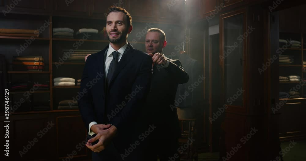 Cinematic shot of young businessman is trying his new custom made high quality tailored suit with designer in luxury tailoring atelier.Concept of fashion, handmade, hand craft, couturier and business.