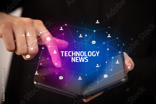 Businessman holding a foldable smartphone with TECHNOLOGY NEWS inscription, new technology concept