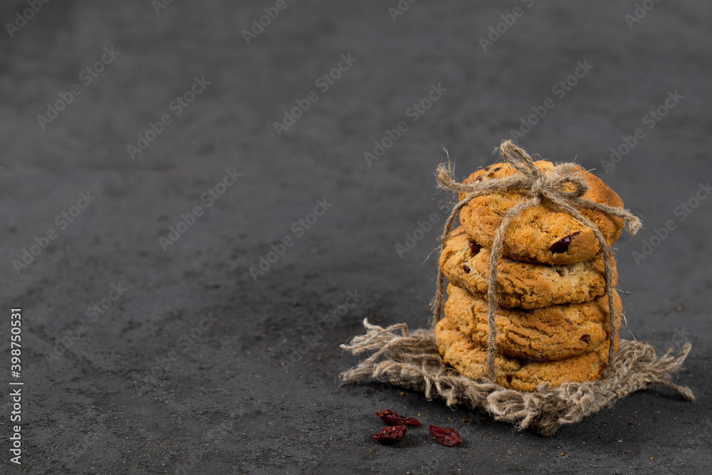 Oatmeal cookies with dried cranberries, tied with jute thread on a linen napkin on a dark gray background in rustic style copy sapce