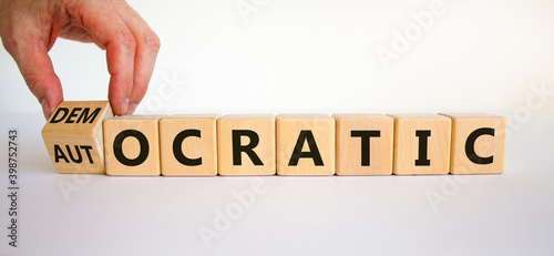 Democratic or autocratic symbol. Male hand turns a cube and changes the word 'autocratic' to 'democratic'. Beautiful white background, copy space. Business and democratic or autocratic concept.
