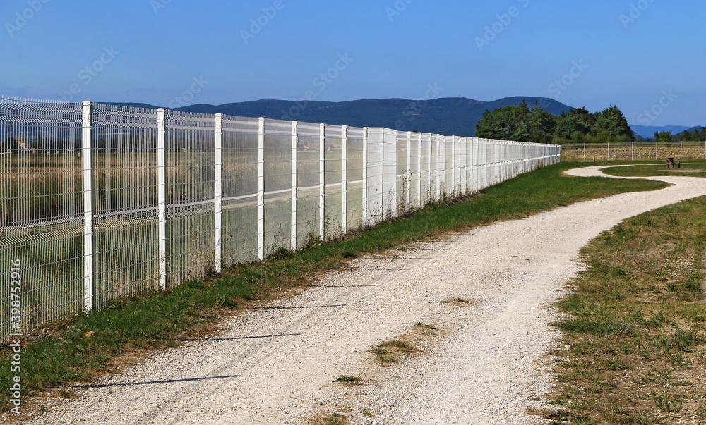 Haute clôture métallique rectiligne et de couleur blanche.