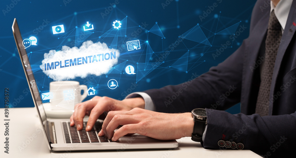 Businessman working on laptop with IMPLEMENTATION inscription, modern technology concept Businessman working on laptop with IMPLEMENTATION inscription, modern technology concept