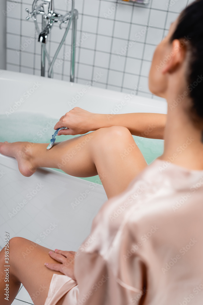 Obraz premium woman shaving leg with razor near bath on blurred background