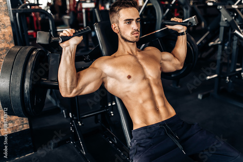 young muscular man, shirtless, working out in the gym, doing chest and arm exercises