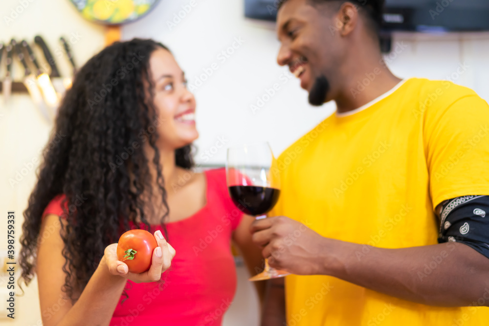 Romantic couple at home. Attractive young woman and handsome man are enjoying spending time together while standing on traditional kitchen. Love and food concept. Focus on tomate.