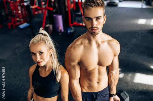 Sporty couple, muscular man and woman, in sportswear, train with dumbbells in the gym