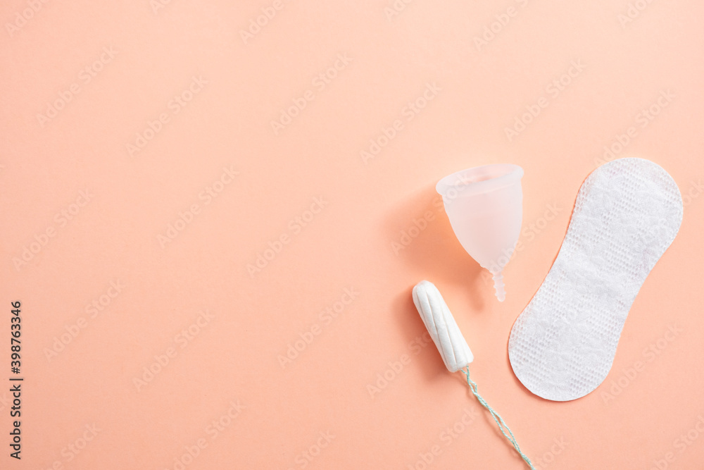Obraz premium Menstrual hygiene products including tampon, menstrual cup and sanitary pad on peach background