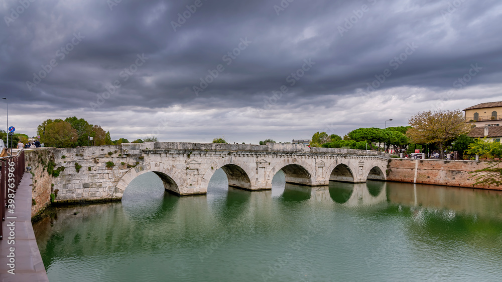 View of the Tiberius Bridge or Ponte di Augusto, a Roman bridge in Rimini, Italy, under a dramatic sky