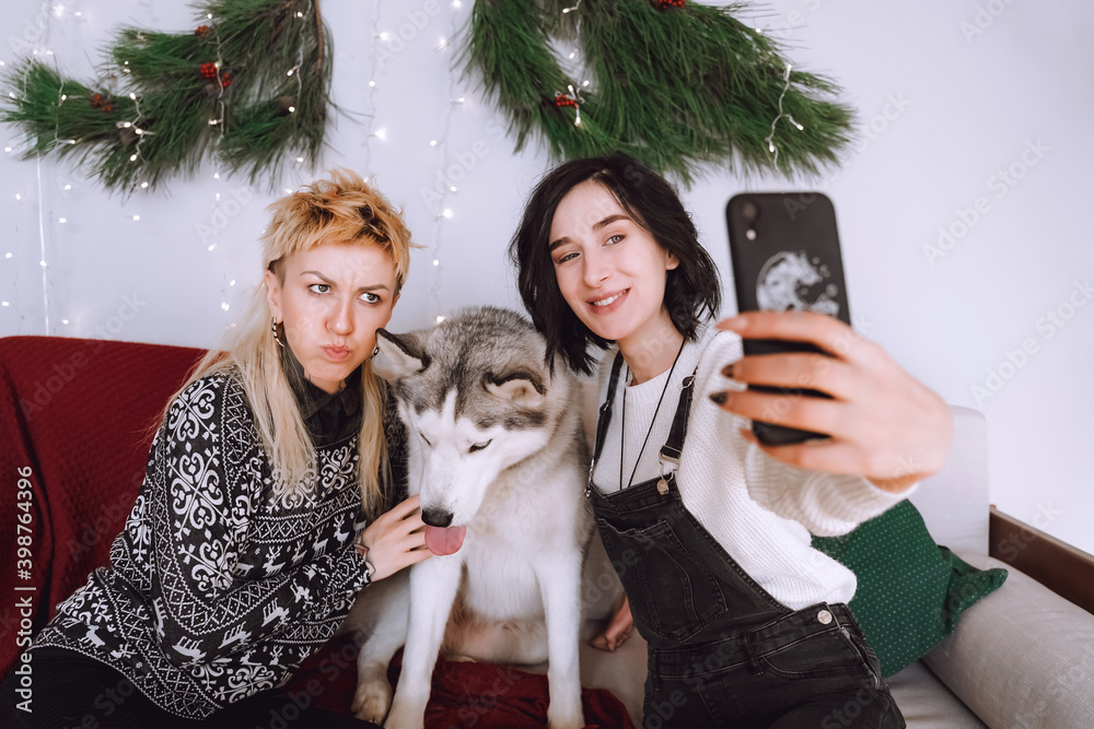 Obraz premium Two happy girls friends or sisters making selfie with white husky dog in Christmas decorations