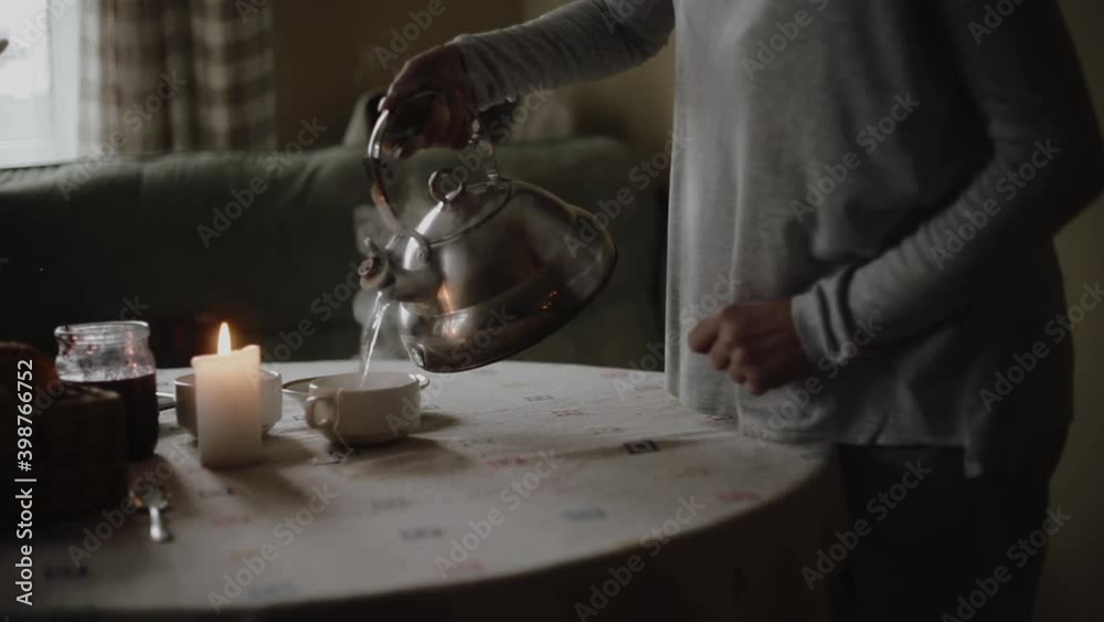 Woman pours hot tea from a teapot into a cup Woman pours hot tea from a teapot into a cup