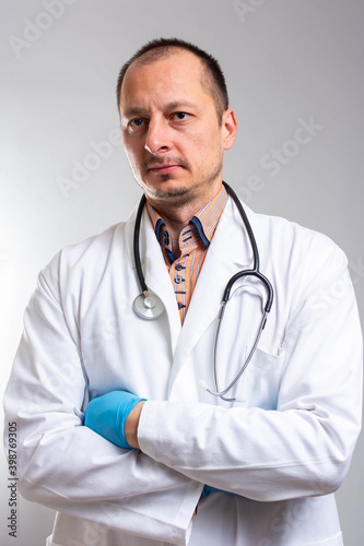 Male doctor in white uniform standing with crossed arms. isolated female portrait. Portrait of happy successful female doctor. Hospital worker looking at camera and smiling, studio, gray background © Nenad