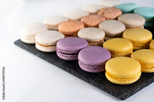 Macarons are laid out on a black slate in beautifully colored rows.