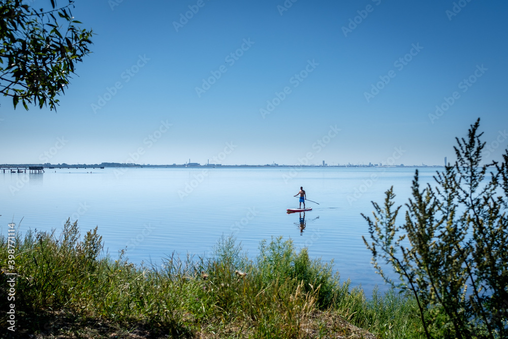 a a lone board sailor in the quiet bay in the southern Öresund, on the Swedish side - SUP stand up paddle board a a lone board sailor in the quiet bay in the southern Öresund, on the Swedish side - SUP stand up paddle board