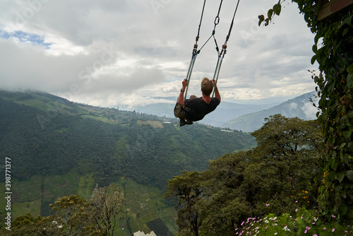 young blond haired caucasian man sitting on a large wooden swing at the tree house, casa del arbol, a popular travel destination, high above Banos in the andes mountains of Ecuador
