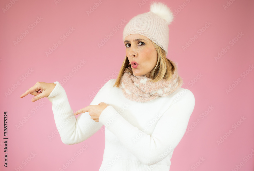Smiling woman wearing winter clothes pointing finger side. Isolated portrait on pink. Smiling woman wearing winter clothes pointing finger side. Isolated portrait on pink.
