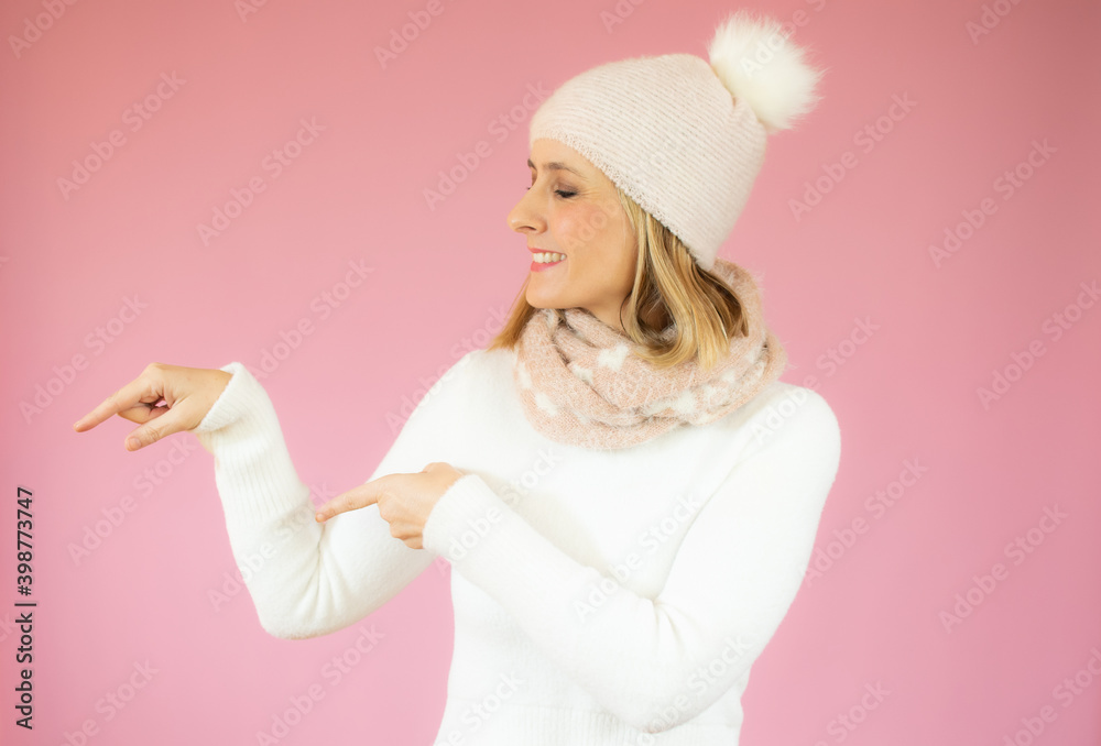 Smiling woman wearing winter clothes pointing finger side. Isolated portrait on pink. Smiling woman wearing winter clothes pointing finger side. Isolated portrait on pink.