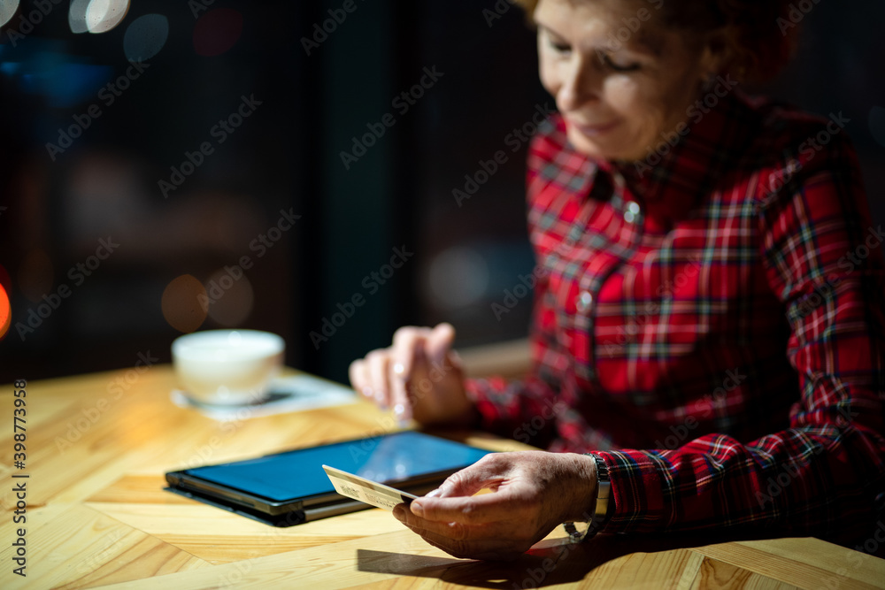 Senior woman ordering Christmas gifts online on digital tablet in coffee shop. Mature buyer holding tablet pc and credit card. Elderly woman shopping online. Online personal finance. Black Friday Senior woman ordering Christmas gifts online on digital tablet in coffee shop. Mature buyer holding tablet pc and credit card. Elderly woman shopping online. Online personal finance. Black Friday