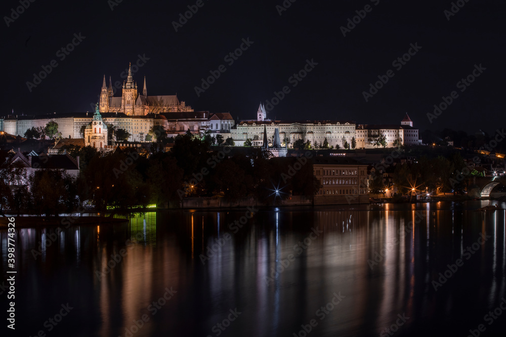 old illuminated prague castle and charles bridge and st. vita church lights from street lights are reflected on the surface of the vltava river in the center of prague at night in the czech republic