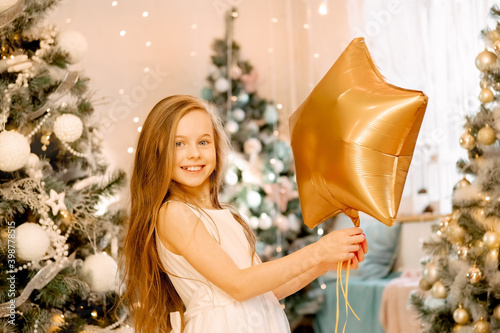beautiful little girl laughs and stands near the Christmas trees with a star balloon. concept of happy childhood, making a wish for the new year and birthday. photo