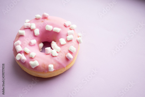 Pink sweet donut with marshmallows on a lilac background. Close-up. Flatley. Place for text and design.