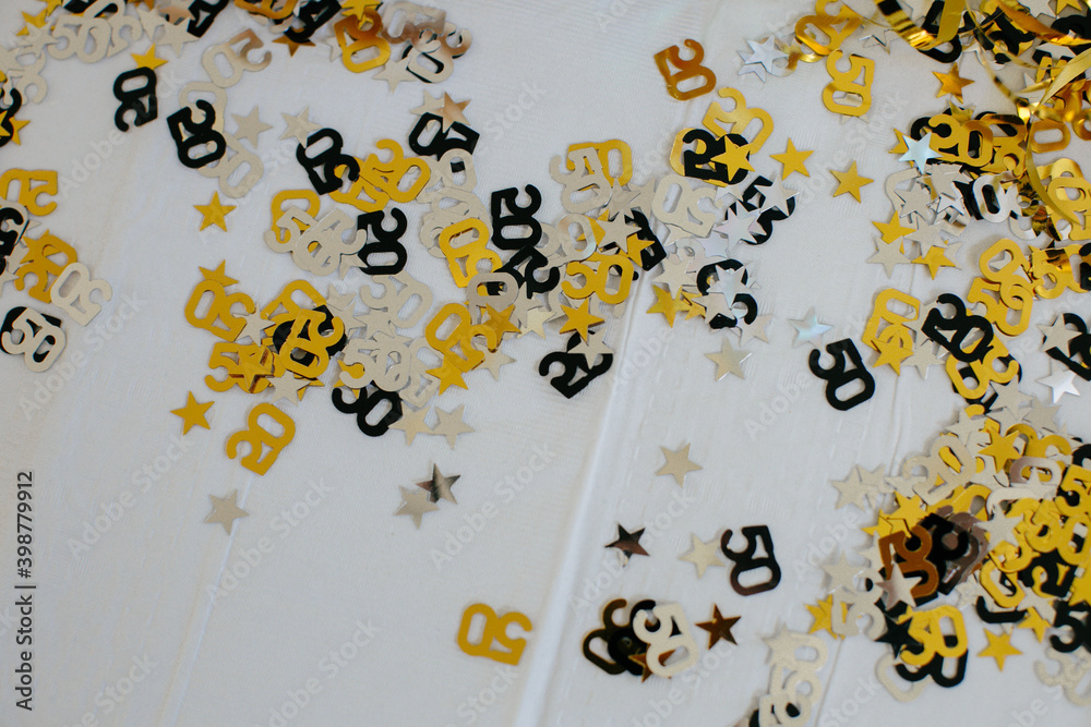 Fiftieth anniversary party black and gold confetti flay lay on table with white tablecloth Fiftieth anniversary party black and gold confetti flay lay on table with white tablecloth