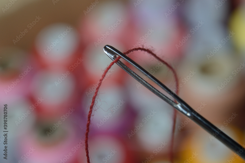 a sewing needle with red thread through the eye of the needle. macro.